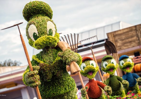 Disney-themed topiary sculptures of Donald Duck and his three nephews, Huey, Dewey, and Louie, depicted as gardeners. Each character is crafted from green foliage, holding gardening tools, with a building and a blue sky in the background.