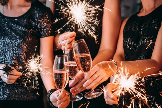 Three people in sparkly outfits clink champagne glasses while holding lit sparklers, creating a festive and celebratory atmosphere.